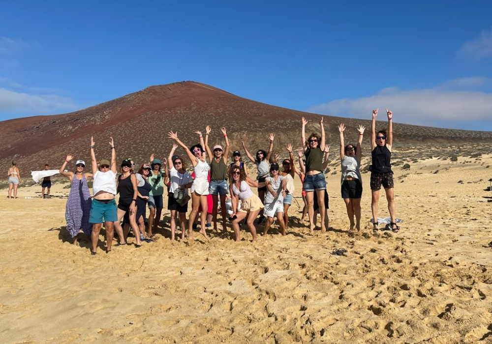 Grupo de mujeres saltando y celebrando al aire libre durante la experiencia Canarias de yoga y bienestar con Lorena Carnevali, en una playa volcánica del archipiélago.