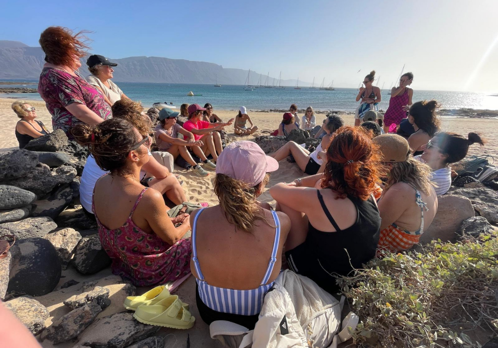Círculo de mujeres sentadas en la arena frente al mar, compartiendo un espacio de escucha, meditación y transformación en la experiencia Canarias de Lorena Carnevali.